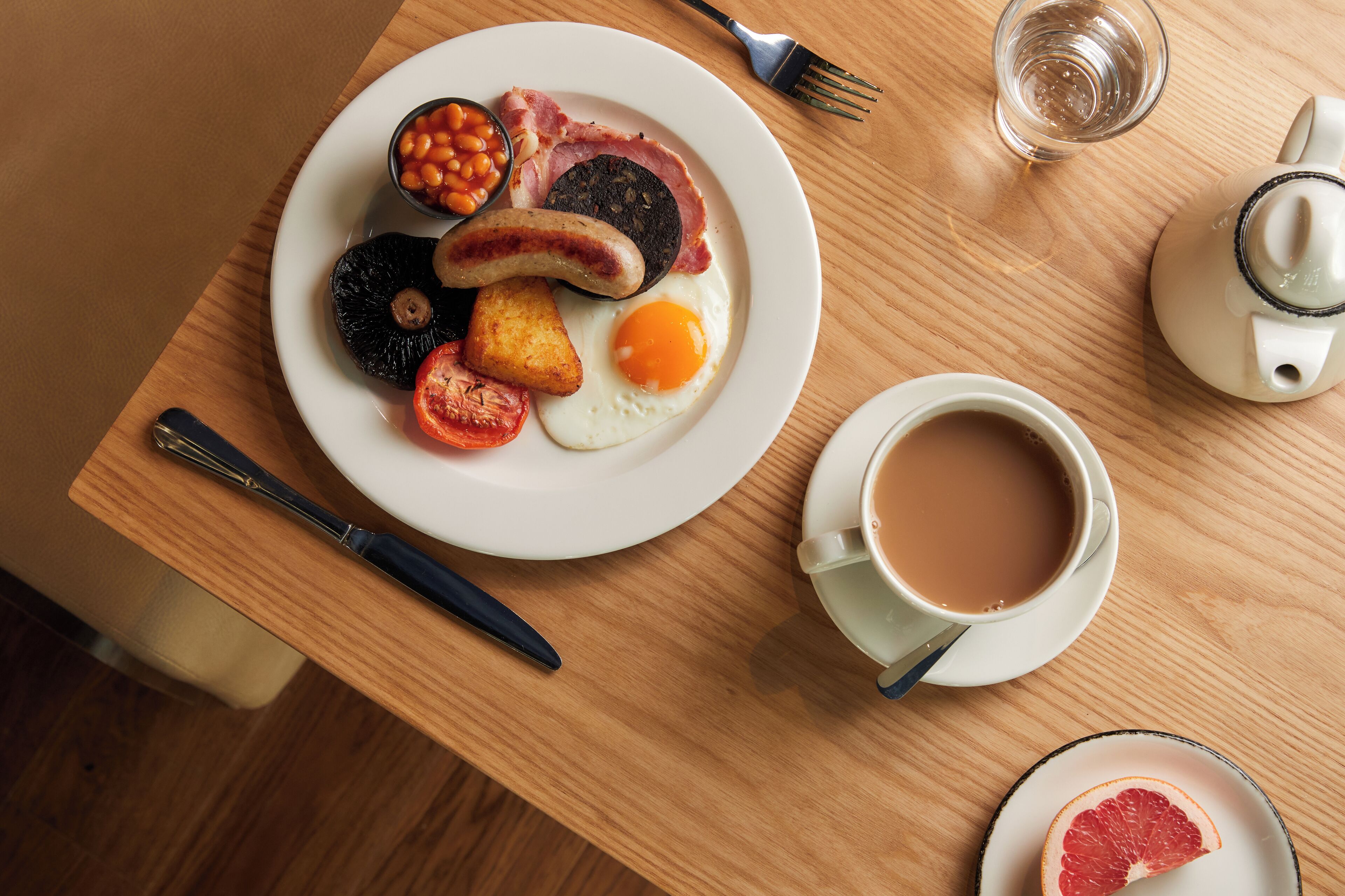 Une assiette de petit-déjeuner avec des œufs, des saucisses, des haricots et des tomates, posée sur une table en bois.