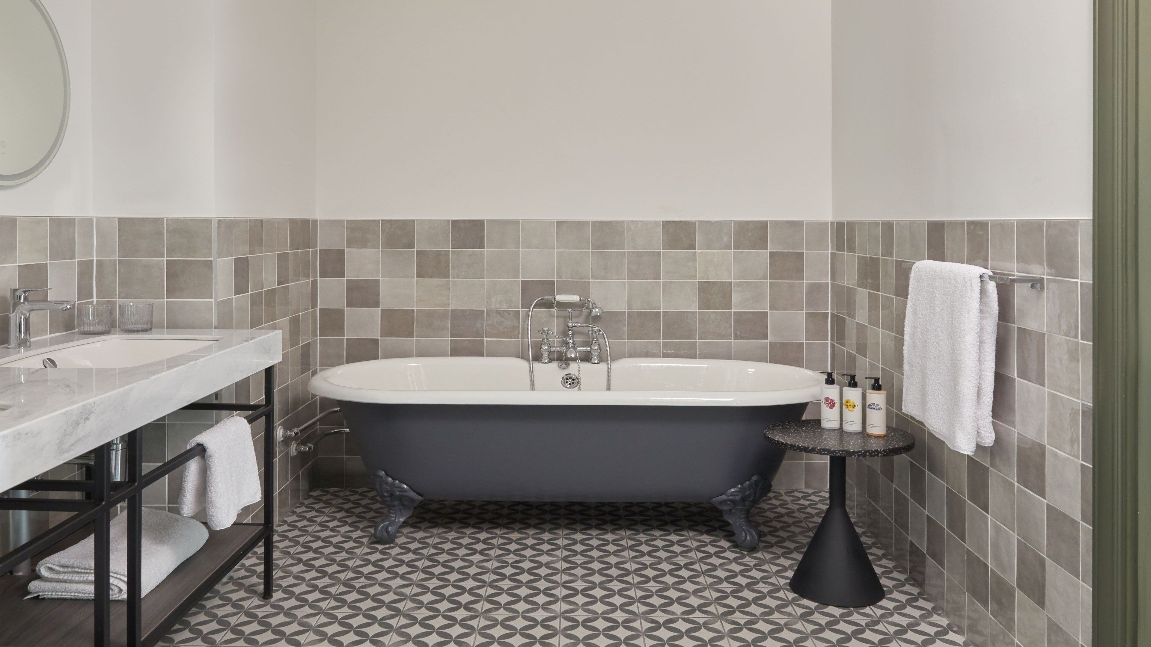 A bathroom with a freestanding bathtub, a vanity with a mirror, and a small round table with toiletries.