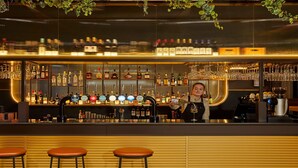 Zona de bar con varias botellas de licores, un bartender y taburetes.