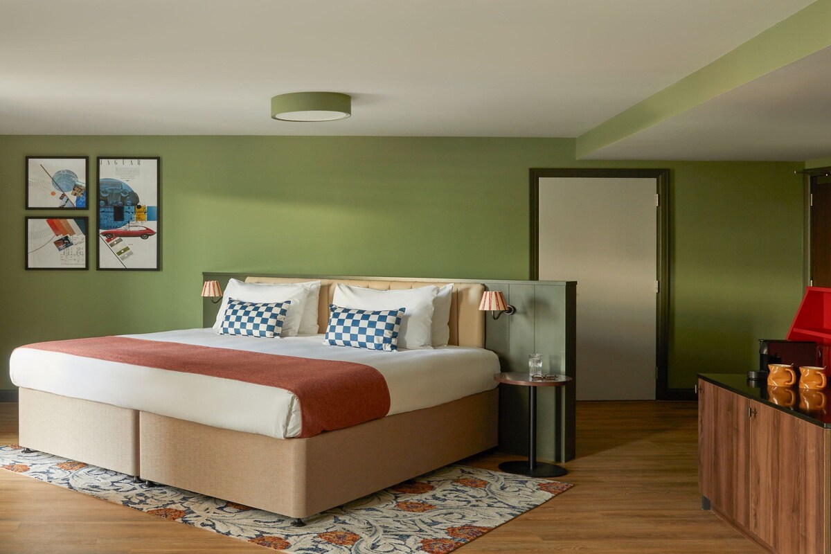 A hotel room with a bed, a nightstand, a lamp, a mirror, and a wardrobe.