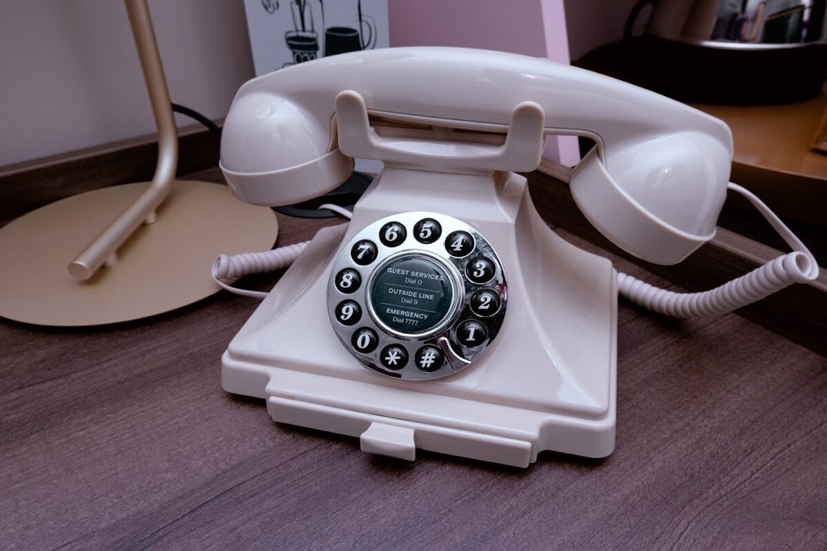 A white rotary dial telephone on a wooden floor.