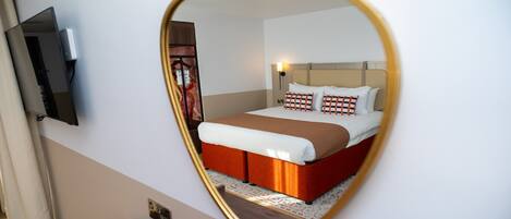 Habitación de hotel con una cama, un televisor montado en la pared y un espejo que refleja la habitación.