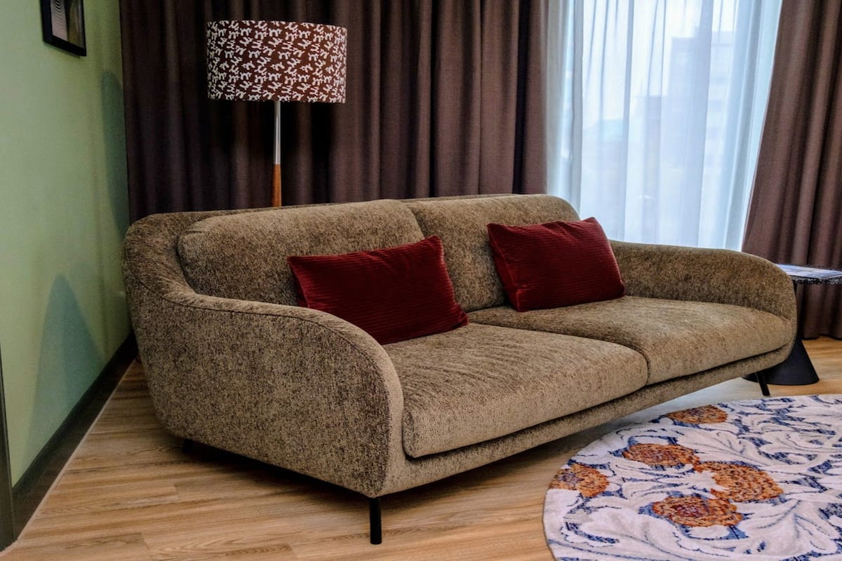 A room with a sofa, two red cushions, a patterned rug, a floor lamp, and a small table.