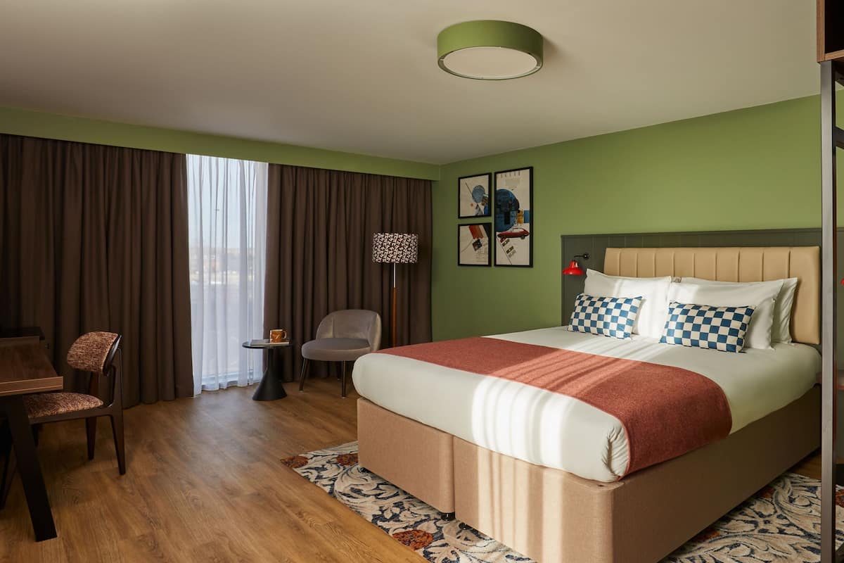 A hotel room with a large bed, a desk, a chair, and a view of the outdoors.