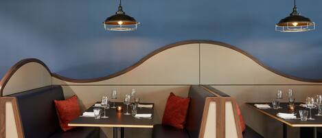 A restaurant interior with booth seating, tables, and hanging pendant lights.