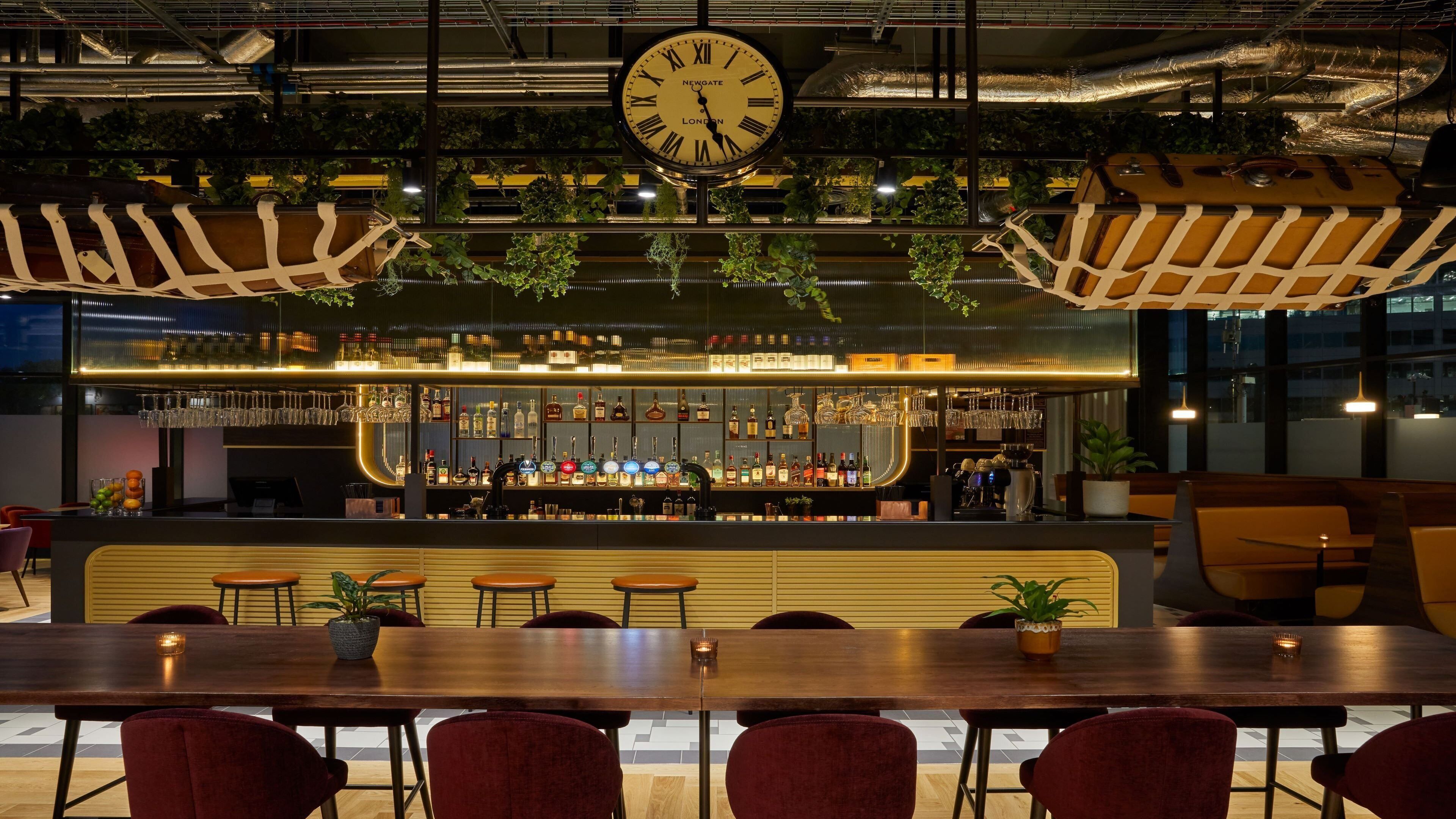 Uma área de bar com um relógio, prateleiras cheias de garrafas e assentos.