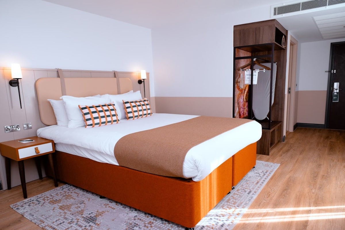 A modern hotel room with a large bed, bedside tables, a wardrobe, and a mirror.