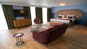 Una habitación de hotel moderna con una cama grande, un sofá, una mesita y un televisor montado en la pared.