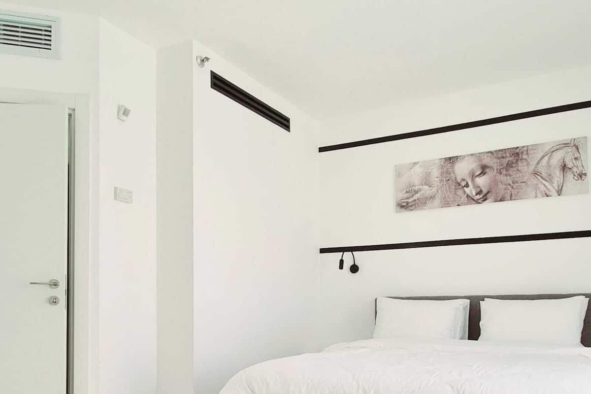 A bedroom with a bed, white walls, a door, and a ceiling vent.