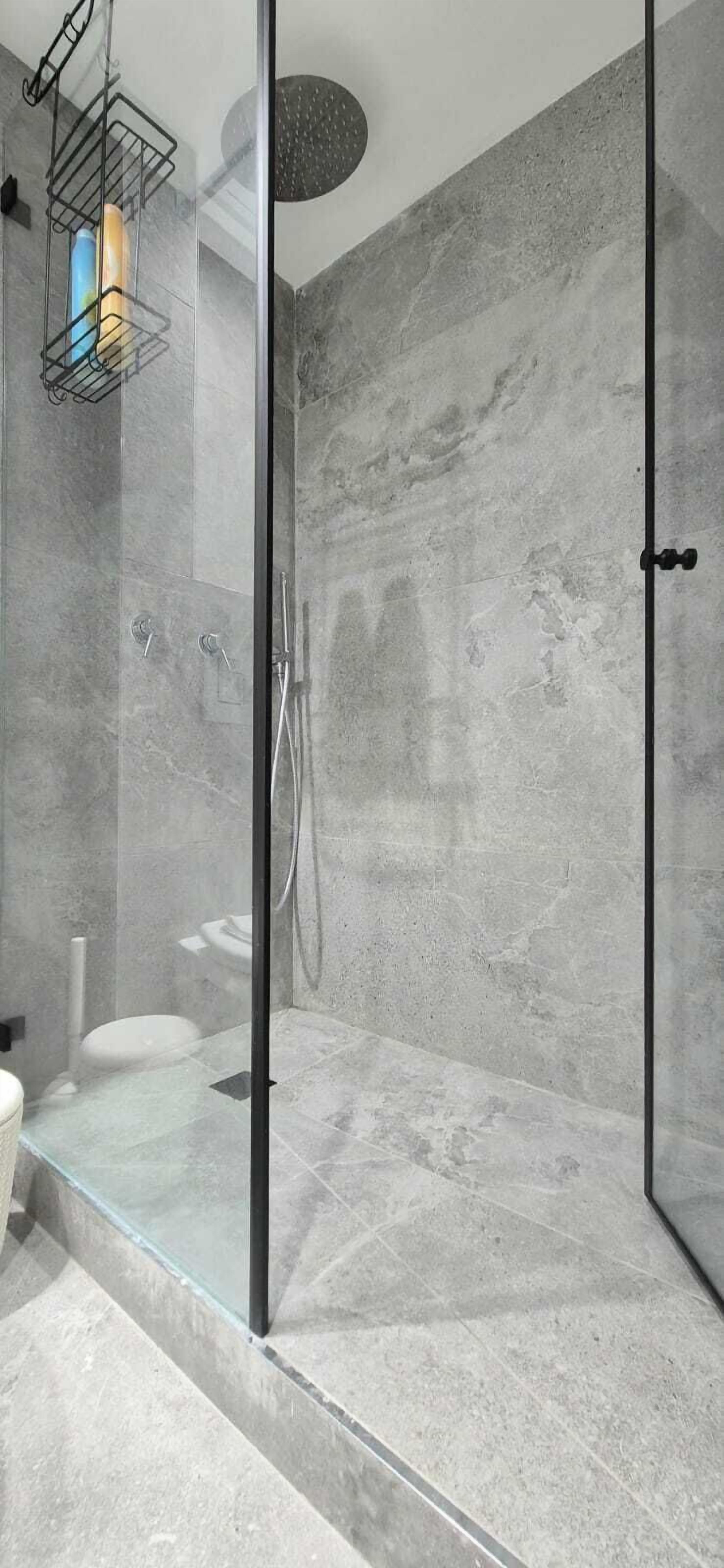 A modern bathroom with a glass-enclosed shower, marble walls, and a visible toilet.