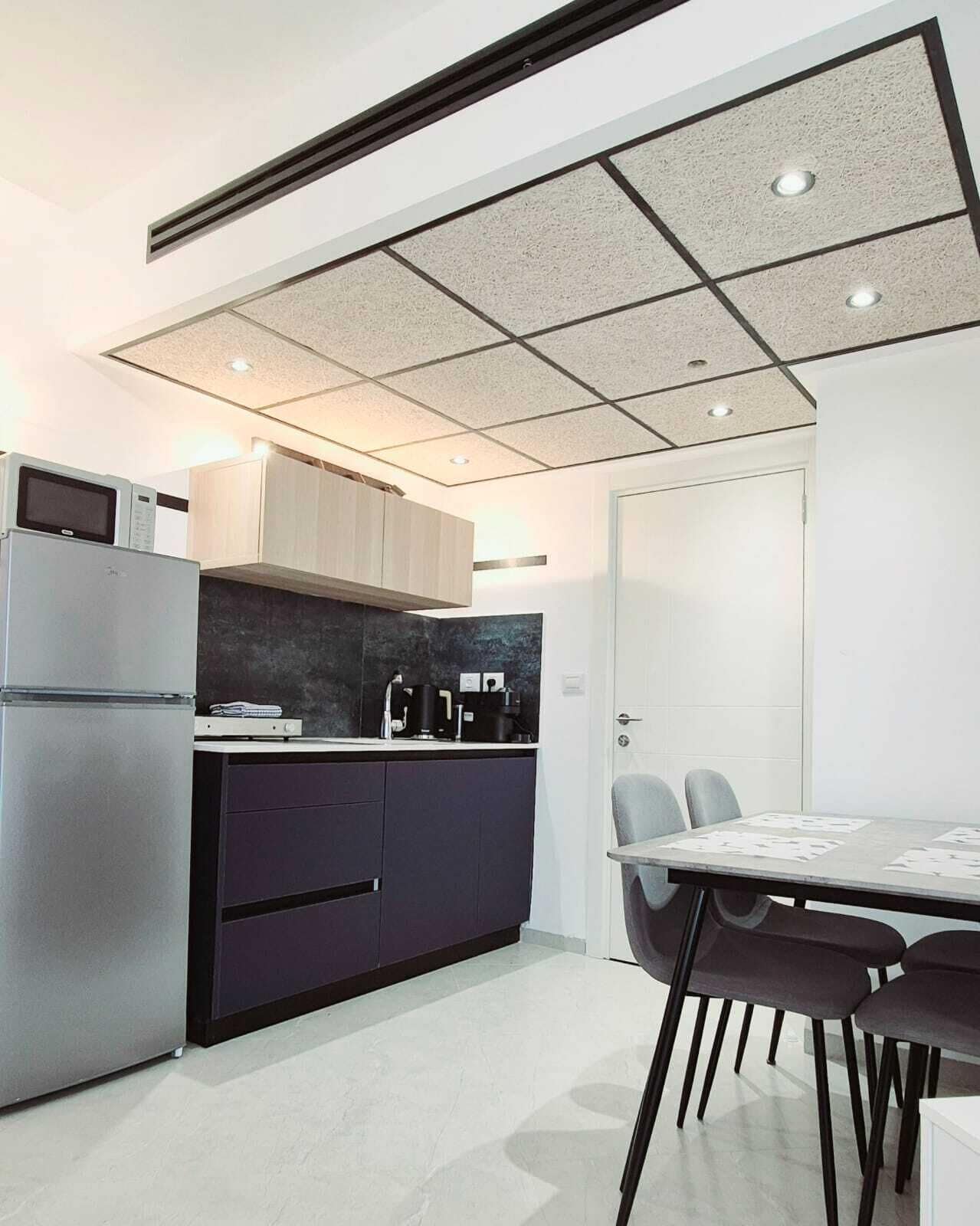 Een moderne keuken met een ingebouwde magnetron, donkere kastjes, een zwart aanrecht en een eethoek met een tafel en stoelen.
