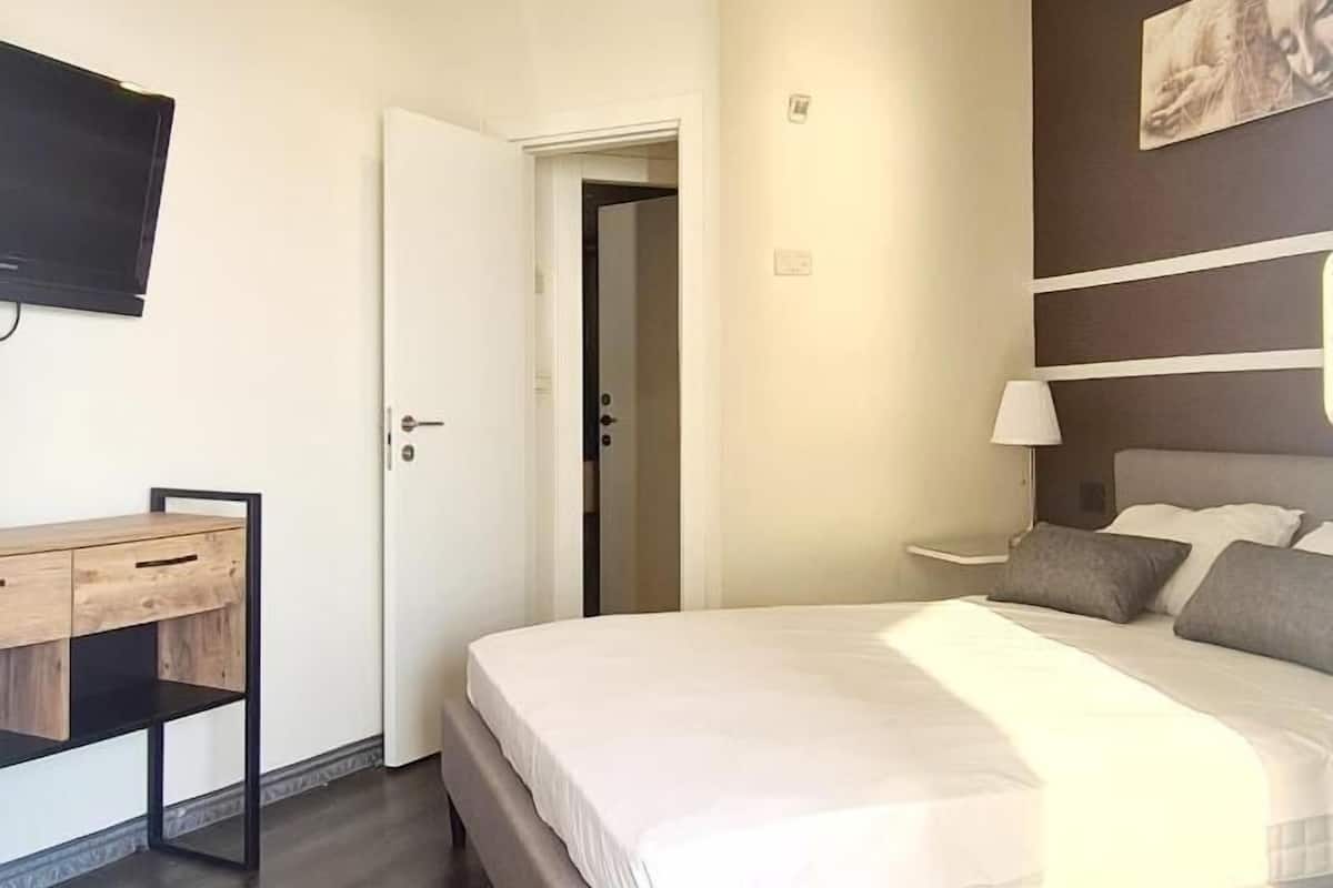 A modern hotel room with a large bed, a desk, a television, and a painting on the wall.