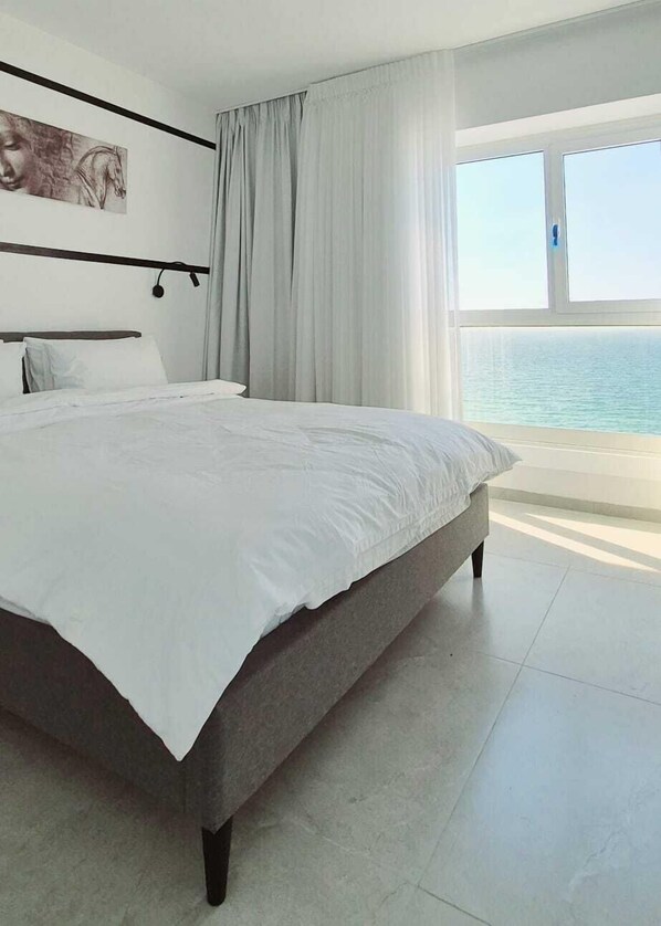 Un dormitorio moderno con una cama grande, vista al mar y un cuadro en la pared.