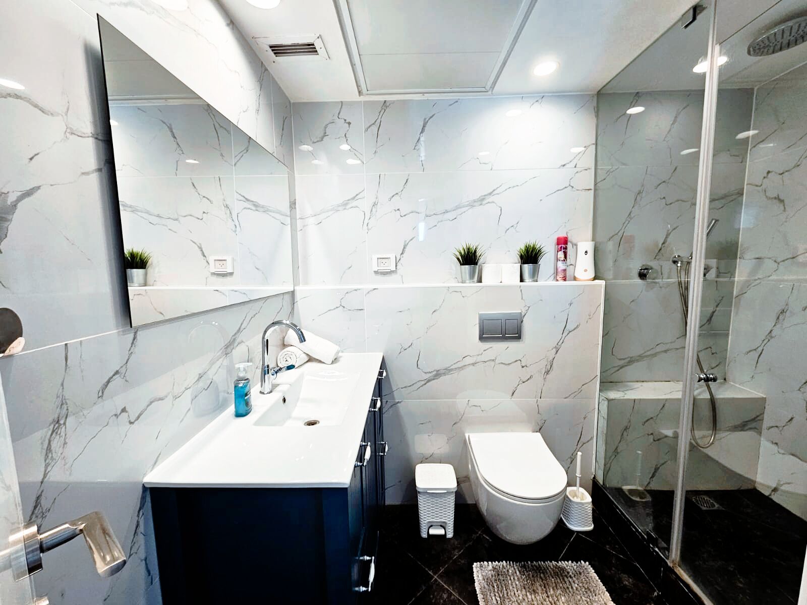 A modern bathroom with a marble backsplash, a white sink, a toilet, and a glass-enclosed shower.