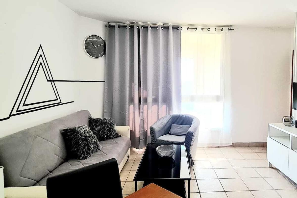 A modern living room with a grey sofa, a black coffee table, a grey armchair, and a white cabinet with a TV.