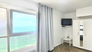 A room with a large window overlooking the sea, a flat-screen TV mounted on the wall, and a small table with a potted plant. - SHaYaSH apartments Leonardo Bat-Yam (Bat Yam)
