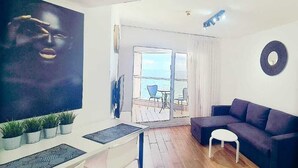 A modern living room with a large window, a sofa, a small table, and a TV. - SHaYaSH apartments Leonardo Bat-Yam (Bat Yam)