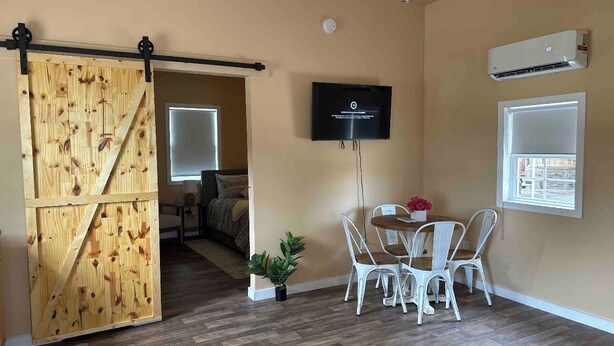 Una habitación con puerta corredera estilo granero, un televisor montado en la pared, una mesa de comedor con sillas y un equipo de aire acondicionado.