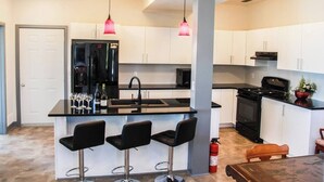 Eine moderne Küche mit einer zentralen Kochinsel, Barhocker, einem Kühlschrank, einem Herd und Pendelleuchten.