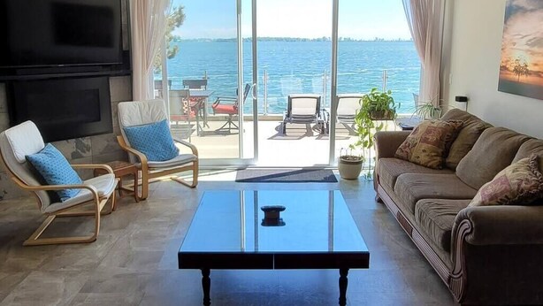 Ein Wohnzimmer mit großem Fernseher, einer Couch, einem Couchtisch und Meerblick durch eine Glastür.