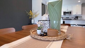 Un comedor con una mesa de madera, un posavasos tejido, una planta en maceta y un panel decorativo.