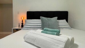 Una cama bien hecha con sábanas blancas, almohadas a rayas y toallas enrolladas.