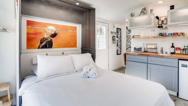 Ein modernes Hotelzimmer mit einem großen Bett, einem Bild an der Wand, einer Küchenzeile inklusive Spüle und Arbeitsfläche sowie einer kleinen Sitzecke.