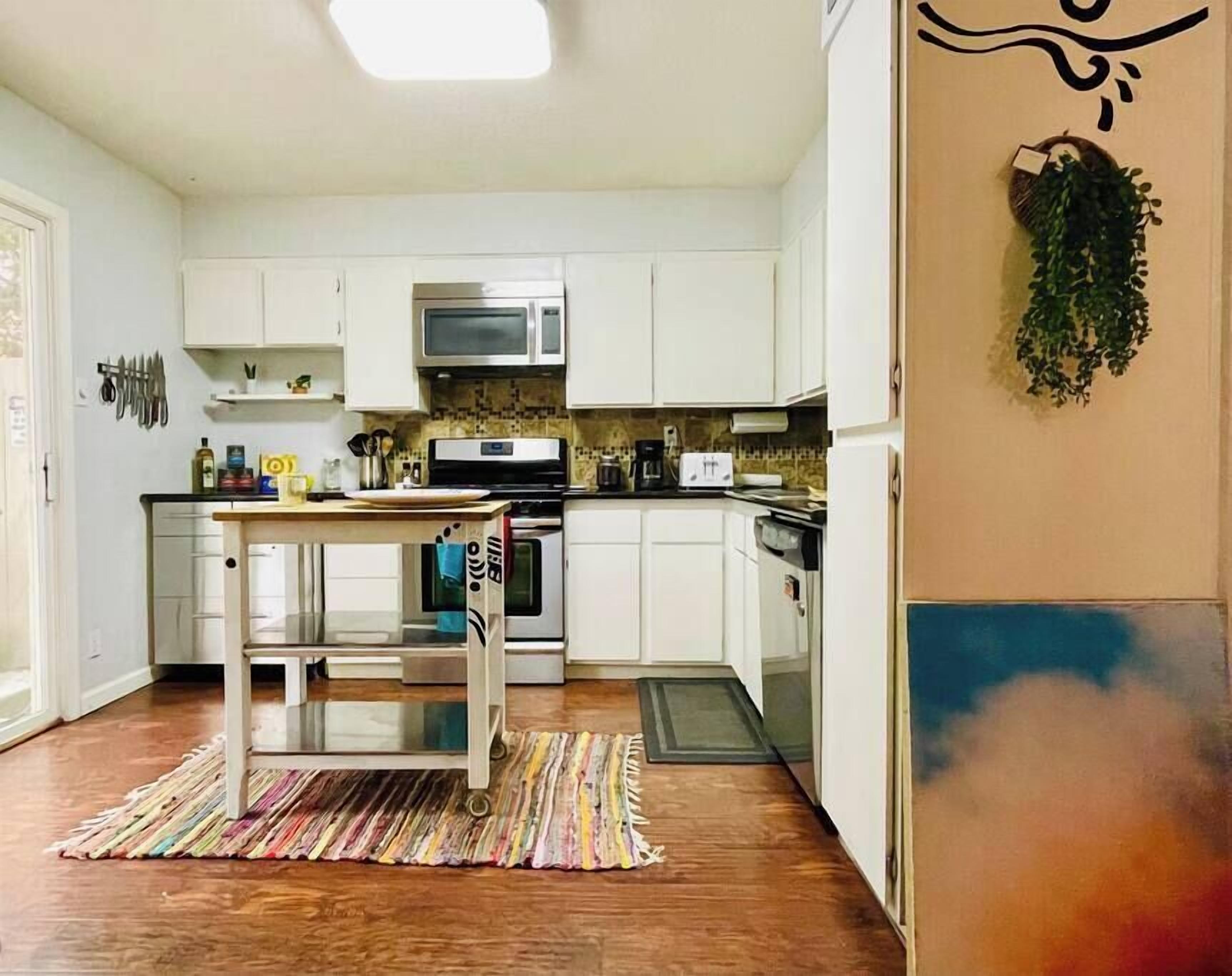 A kitchen with white cabinets, a microwave, a stove, and a sink. There is a colorful rug on the floor.