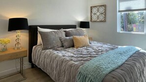 Une chambre à coucher comprenant un lit, deux tables de chevet, une fenêtre et un élément décoratif mural.