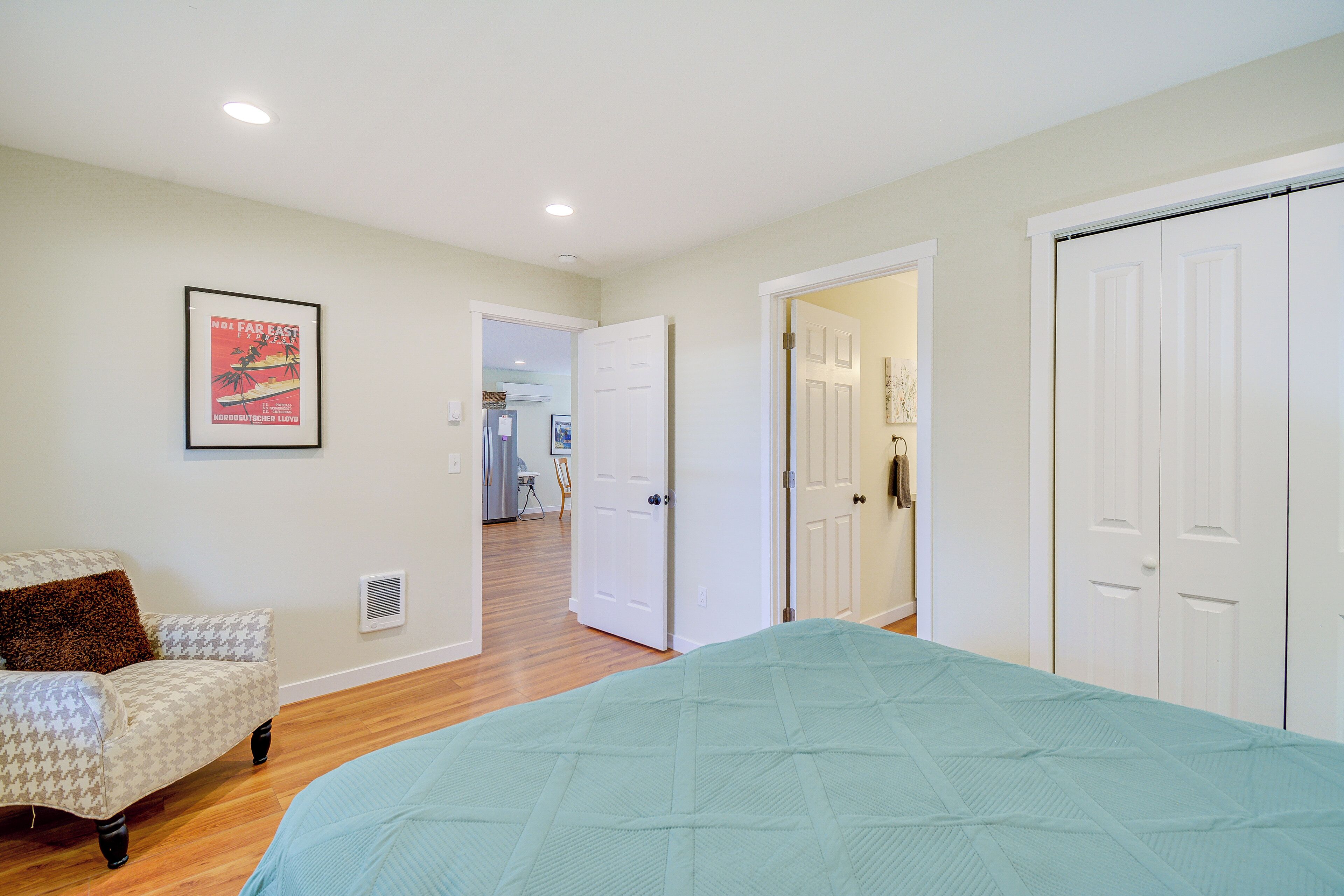A bedroom with a bed, a chair, and a door leading to another room.