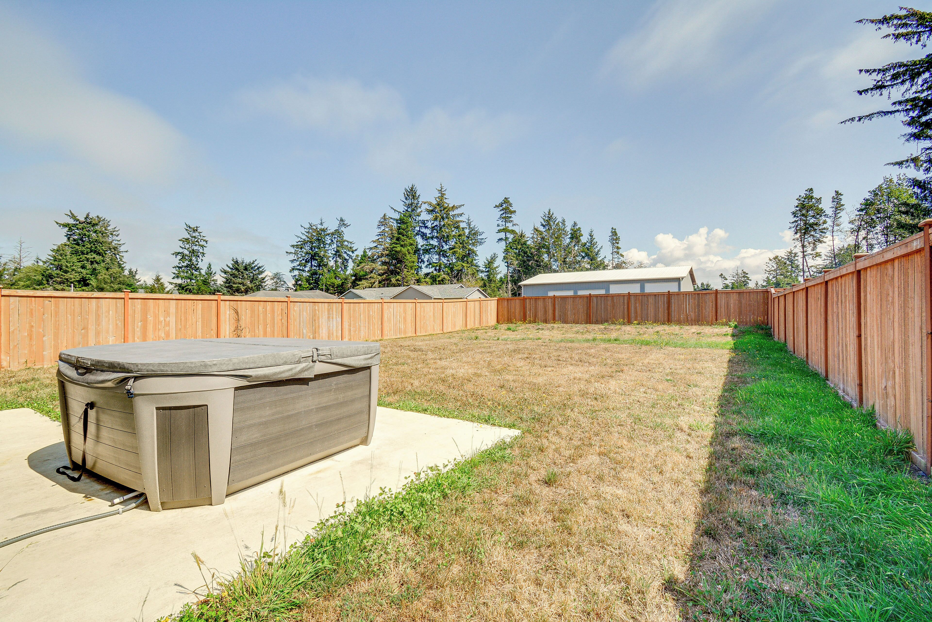 Un jardin avec un jacuzzi, une clôture en bois et un bâtiment visible au fond.