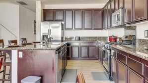 Eine moderne Küche mit dunklen Holzschränken, Edelstahlgeräten, Granit Arbeitsplatten und einer zentralen Kochinsel mit Sitzgelegenheit.