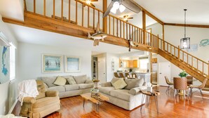 A spacious living area with a wooden staircase, a dining area with a table and chairs, and a kitchen in the background.