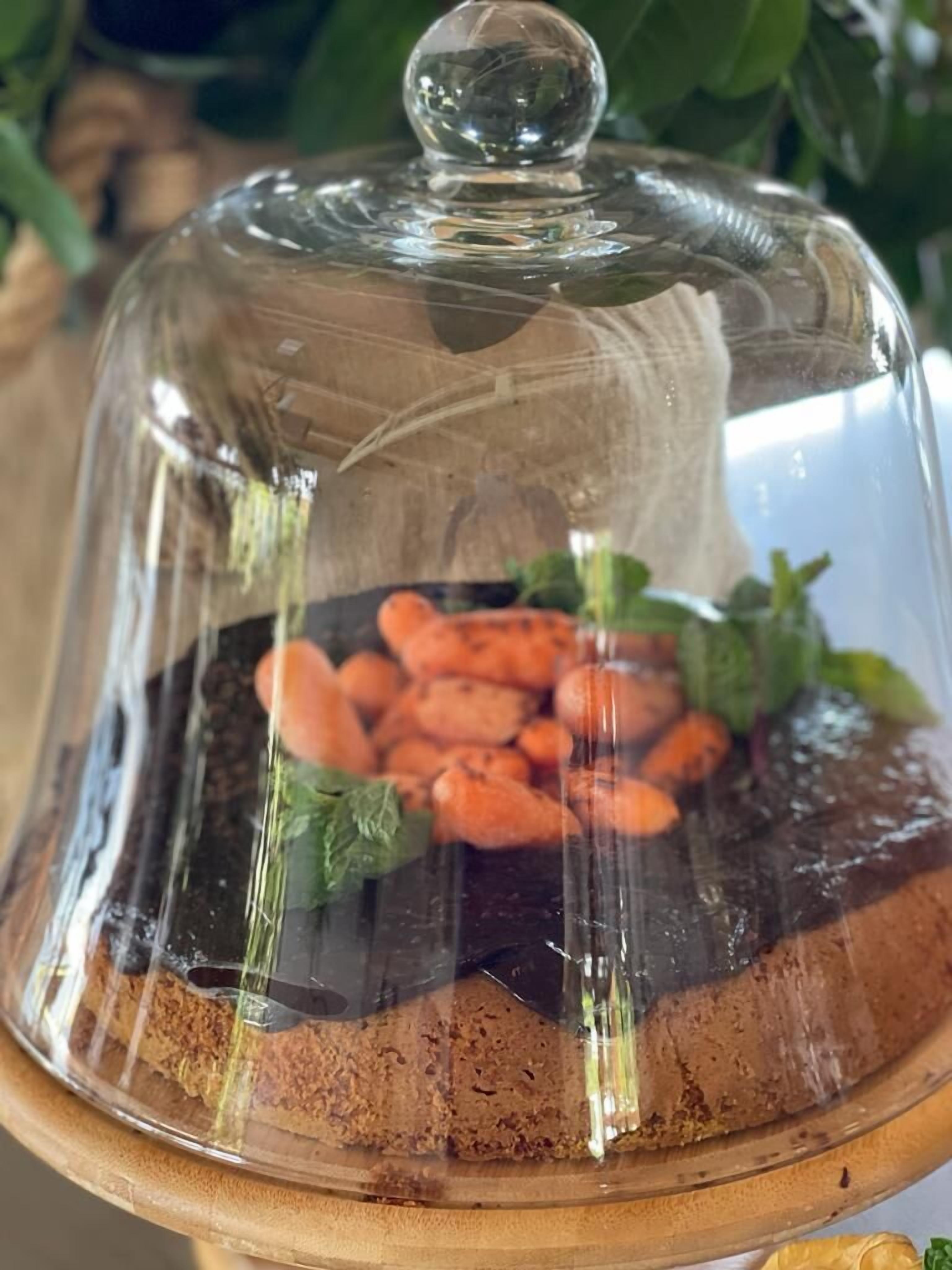 A dessert under a glass dome with a wooden base.