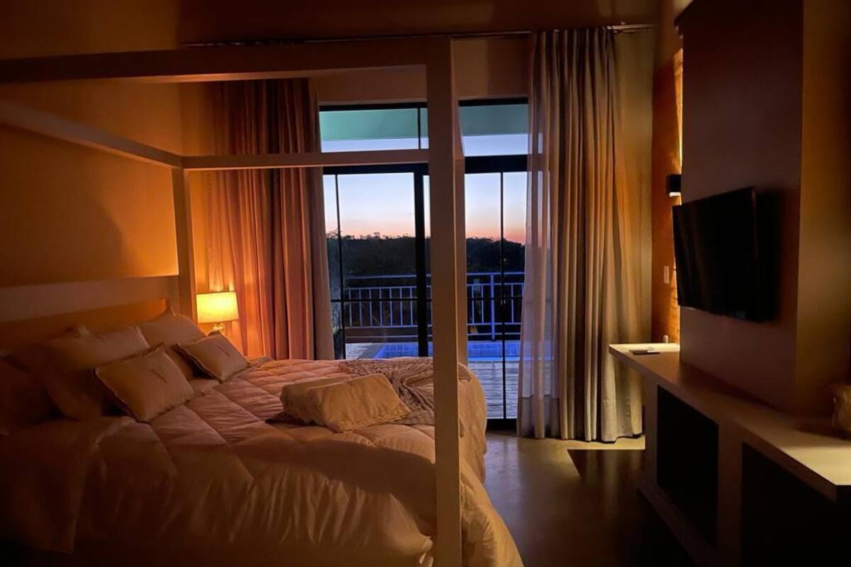 A hotel room with a large bed, a TV, and a balcony with curtains.