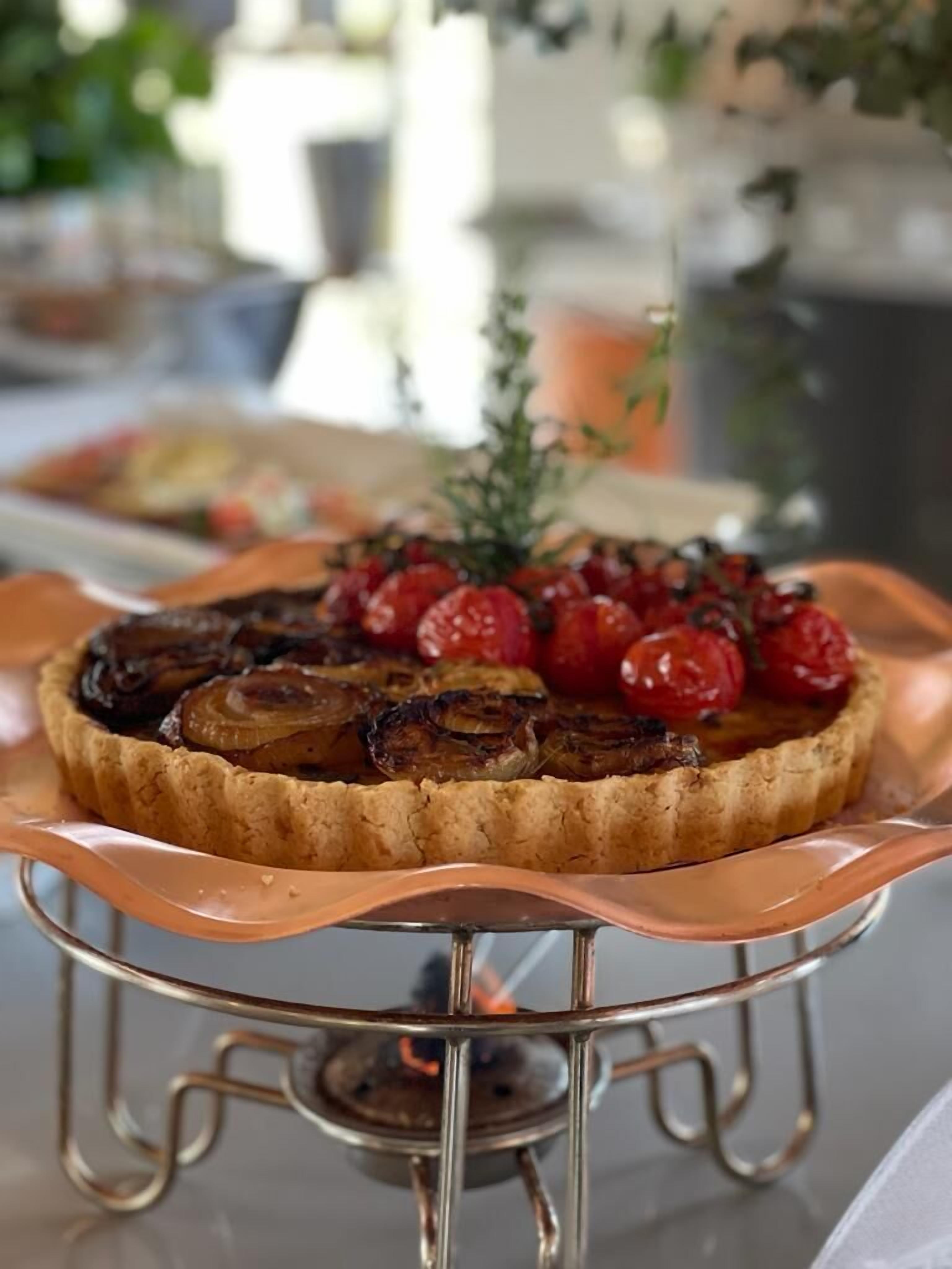 A tart with caramelized onions and cherry tomatoes on a copper serving stand.