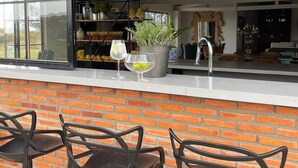 Fachada de ladrillo con zona de bar que incluye tres taburetes y una ventana con vistas a un jardín.