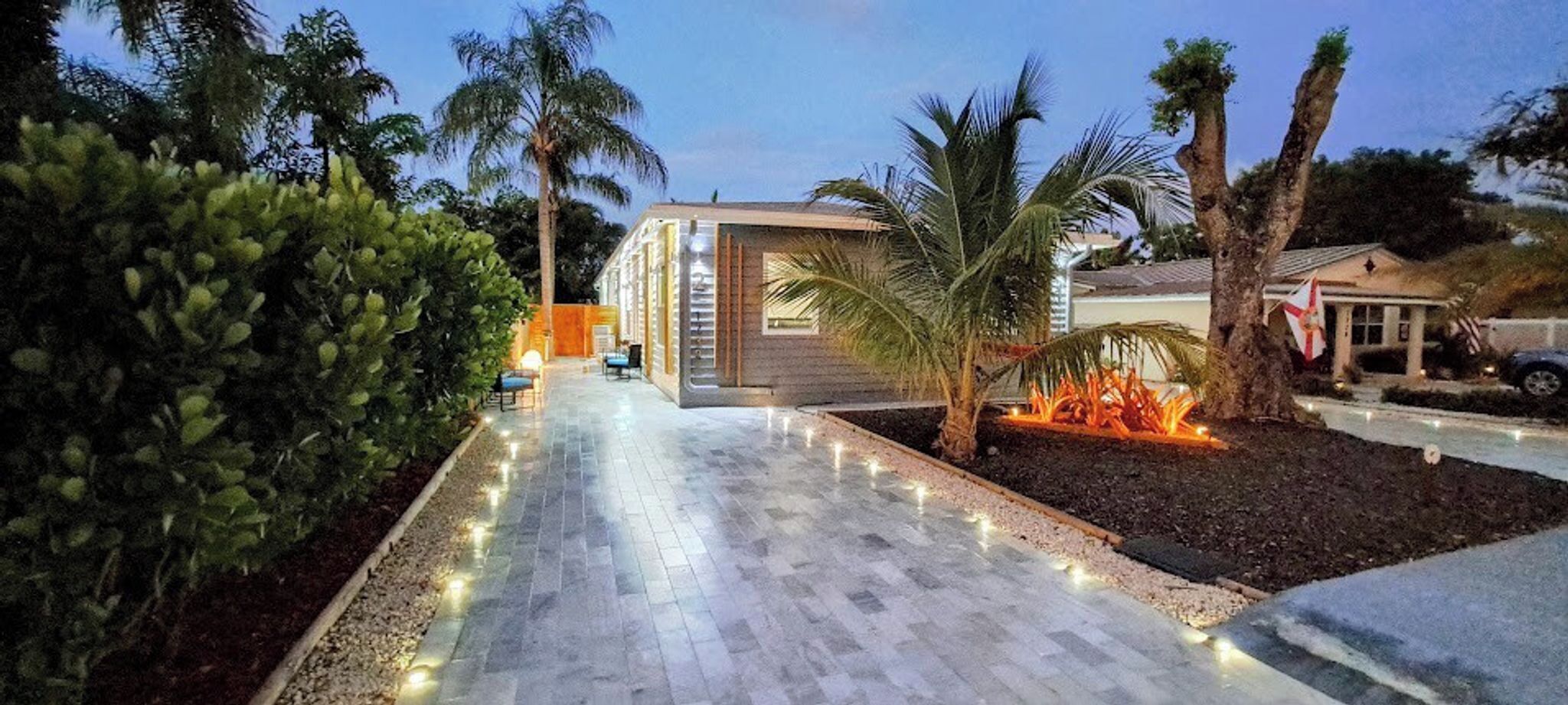 A modern building with a paved walkway, palm trees, and a flag.