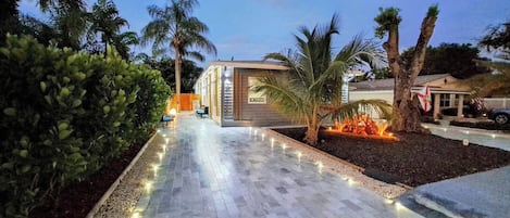 A modern building with a paved walkway, palm trees, and a flag.