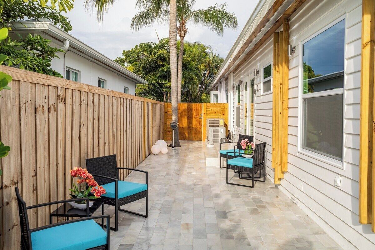 Eine Terrasse mit zwei Stühlen und einem Tisch, ein Holzzaun und ein Haus mit großen Fenstern.