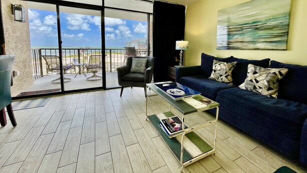 A living room with a blue sofa, a coffee table, and a view of the beach through a sliding glass door.