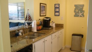 A kitchen with granite countertops, a dishwasher, a coffee maker, and a trash can.