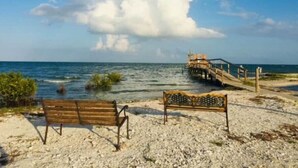 A beach with a wooden bench and a metal bench facing the ocean.