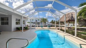 A covered swimming pool with a clear view of a building and palm trees in the background. - Super Snapper OceanView Heated Pool, Tiki, Large Dock, Lanai (Marathon)
