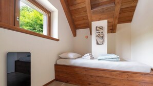 Een slaapkamer met een schuine plafond, een raam met uitzicht op groen, een bed met kussens en handdoeken, en een kunstwerk aan de muur.