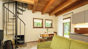 Un espacio habitable compacto con una escalera de madera, un comedor con mesa y sillas, un sofá verde y una cocina con encimera y armarios.
