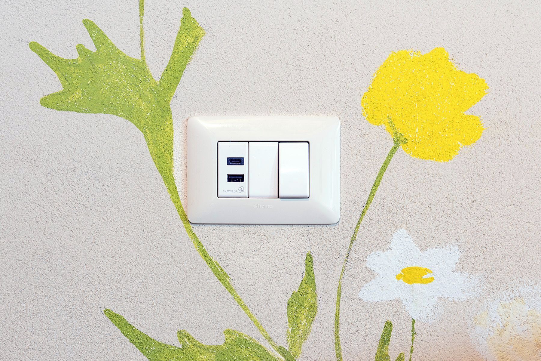 Een lichtschakelaar met twee knoppen en een USB-aansluiting, omringd door bloemenmotieven.