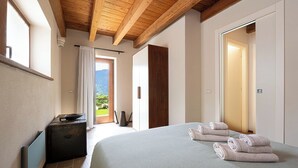 A bedroom with a bed, towels, a wooden wardrobe, a radiator, and a view of greenery outside. - Baita Athili - Crodini Village (Piemonte)