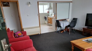 Ett kompakt vardagsrum med en röd soffa, ett träbord, en tv och ett litet kök i bakgrunden.