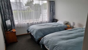 Ett hotellrum med två sängar, en tv på ett träställ, en lampa på ett nattduksbord och tunna, genomskinliga gardiner vid fönstret.